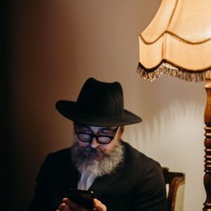 man in hat wearing glasses reading phone alone