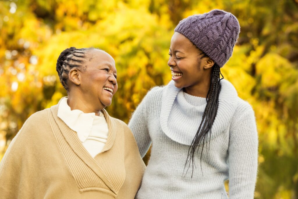 Photo of a Black woman and her daughter outdoors, smiling at one another.