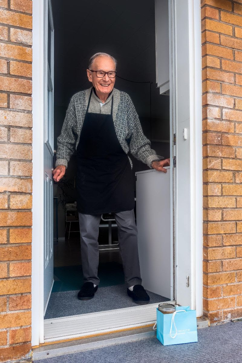 Elderly man standing at front door of home