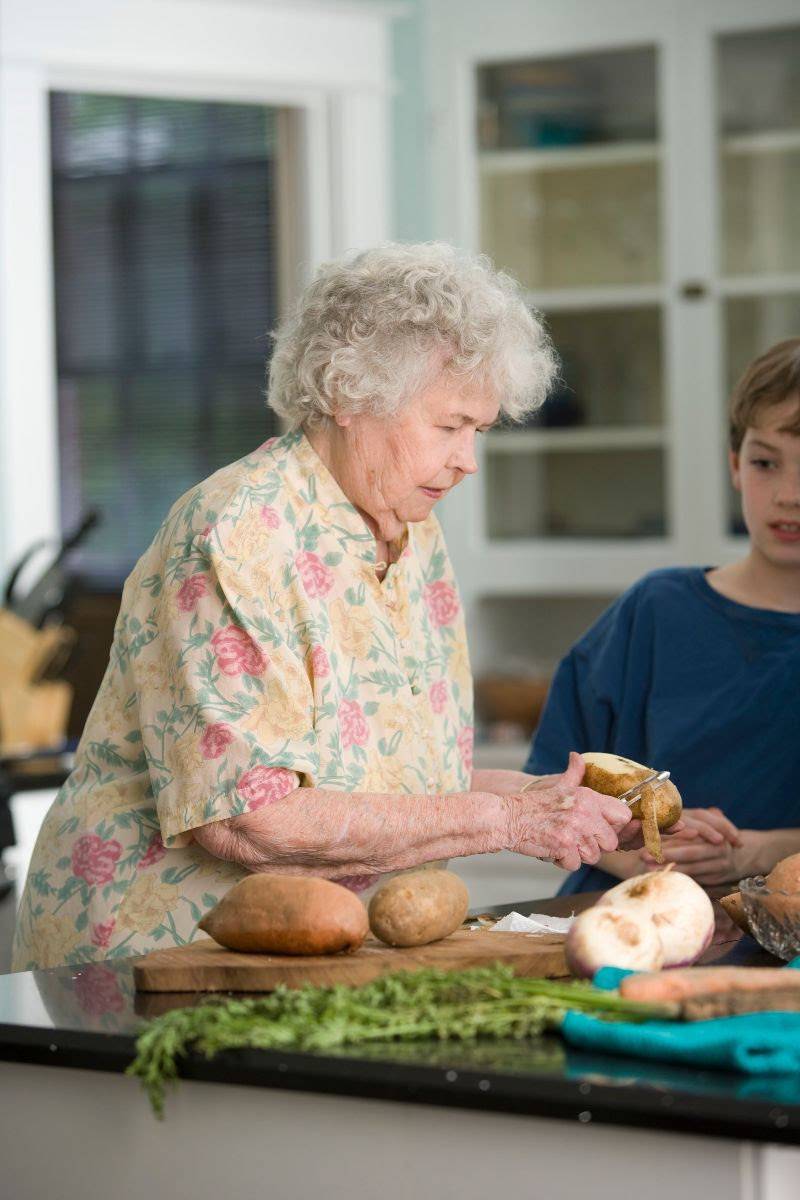 Elderly woman peeling potatoes with grandson watching